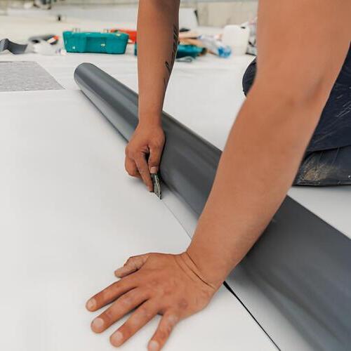 worker laying down a roll of TPO roofing